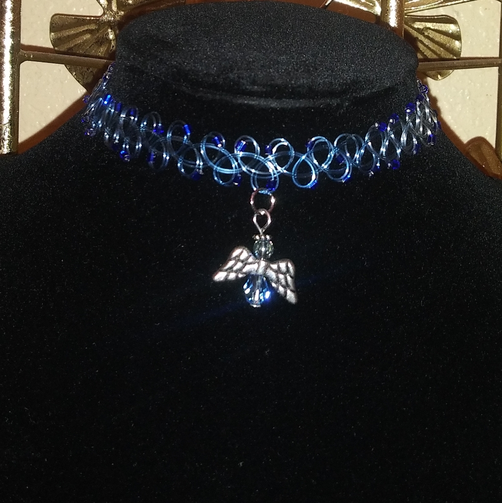 Single black tattoo choker with a small silver angel charm displayed on a black velvet bust